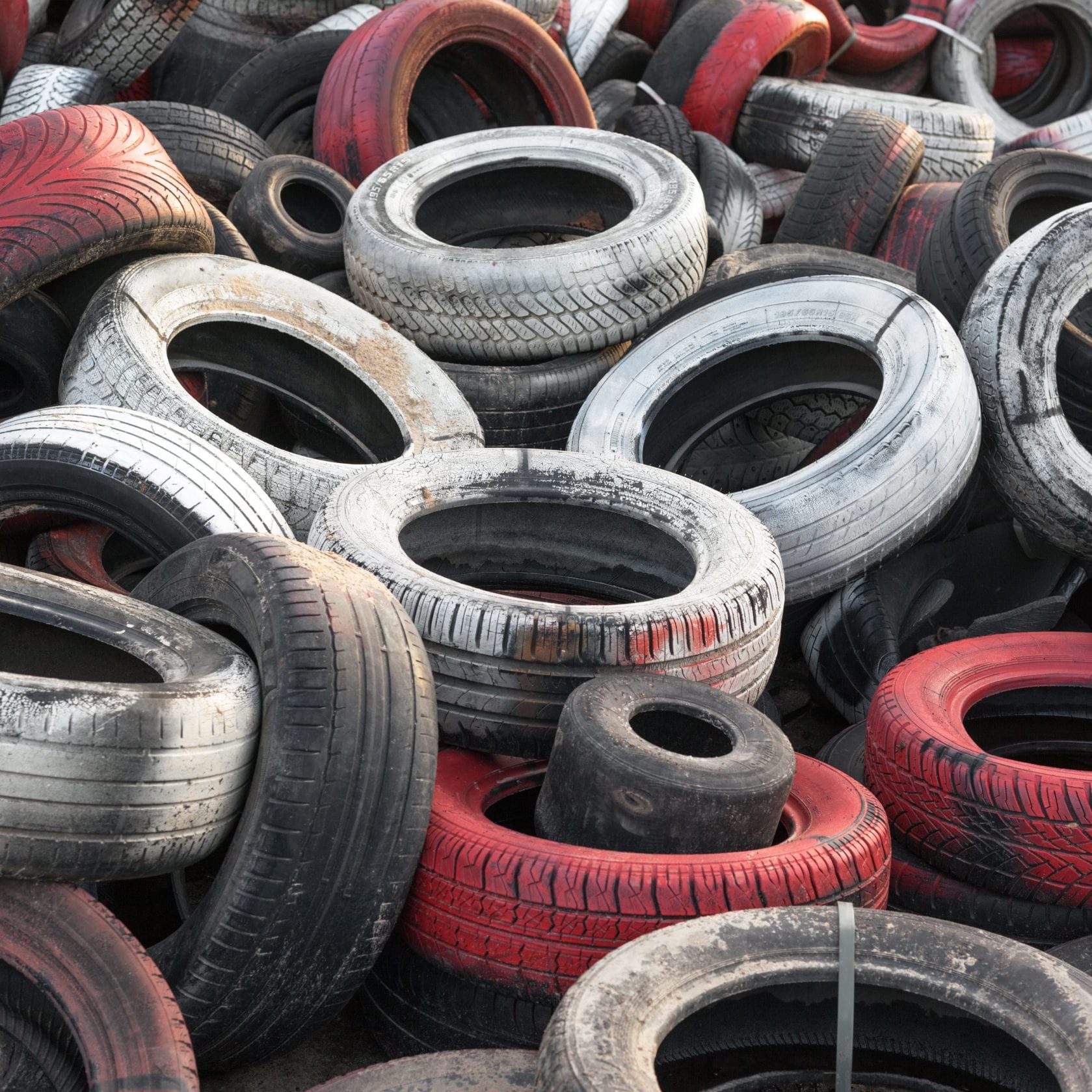 Variety of red white and black waste car tires piled in a big pile